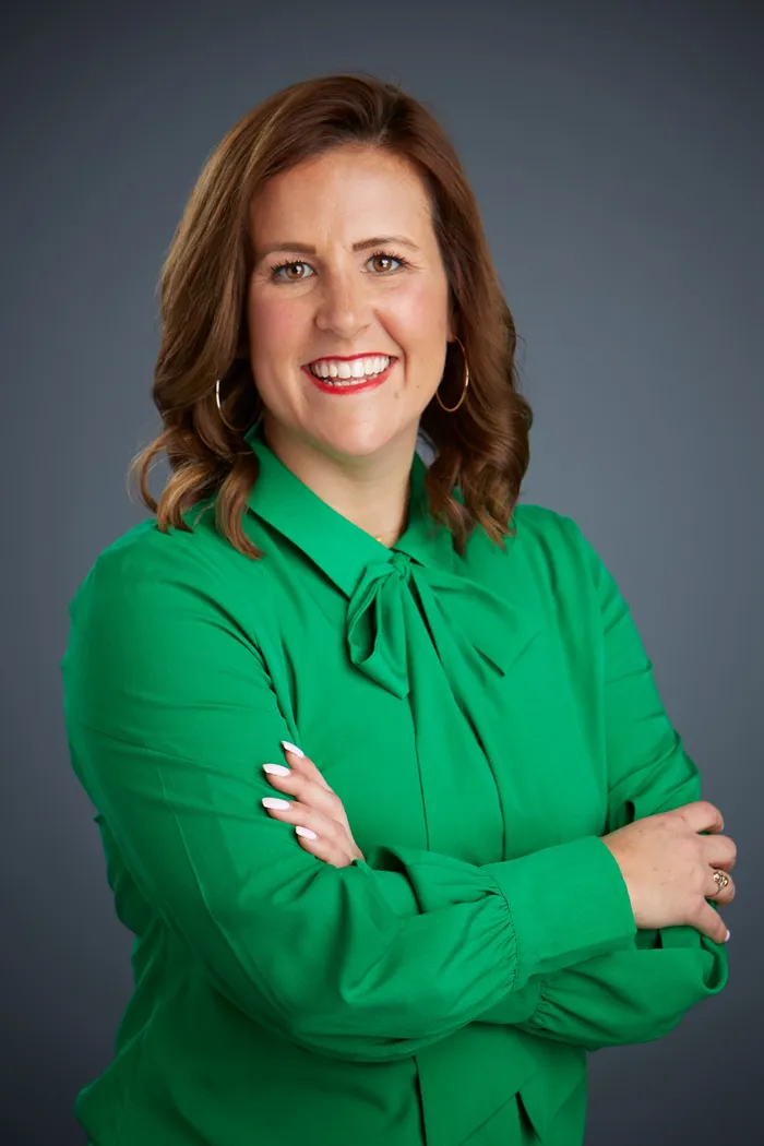 Studio portrait of a woman in a green bow-neck blouse, arms crossed, smiling