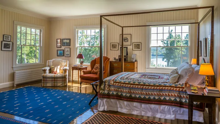 Bedroom with a four-poster canopy bed and large windows overlooking a lake