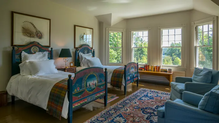 Bedroom with twin painted beds, patterned rug, and a bay of windows