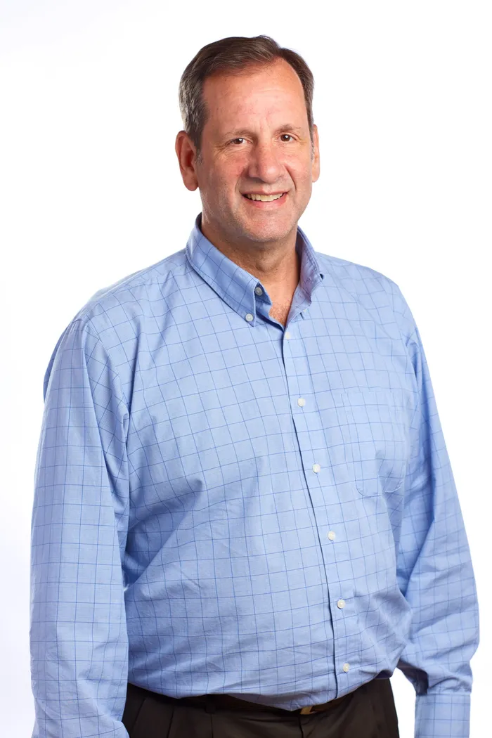 Studio portrait of a man in a light blue checked shirt, smiling, on a white background