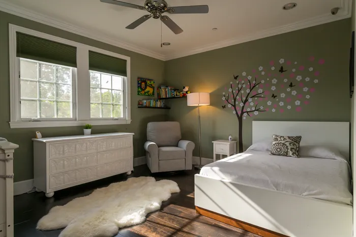 Sage green children's bedroom with a ceiling fan and dresser