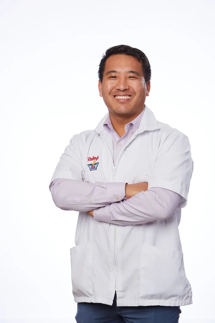 Studio portrait of a man in a white pharmacy lab coat, arms crossed, smiling