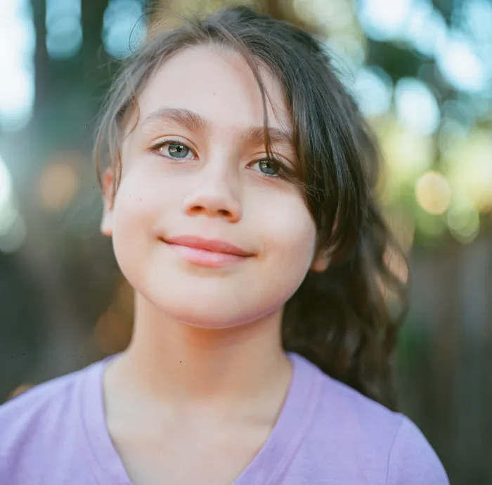 Outdoor portrait of a young girl smiling, soft natural light with trees in the background