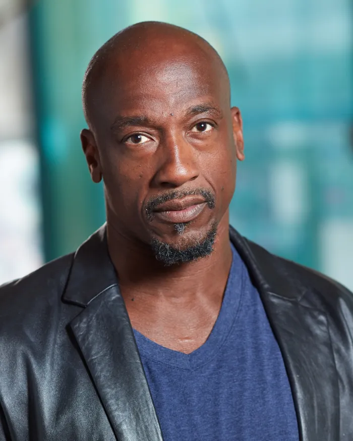 Studio portrait of a bald man with a goatee in a leather jacket, against a blurred colorful background