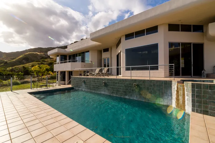 Modern hillside home exterior with an infinity-edge pool at dusk