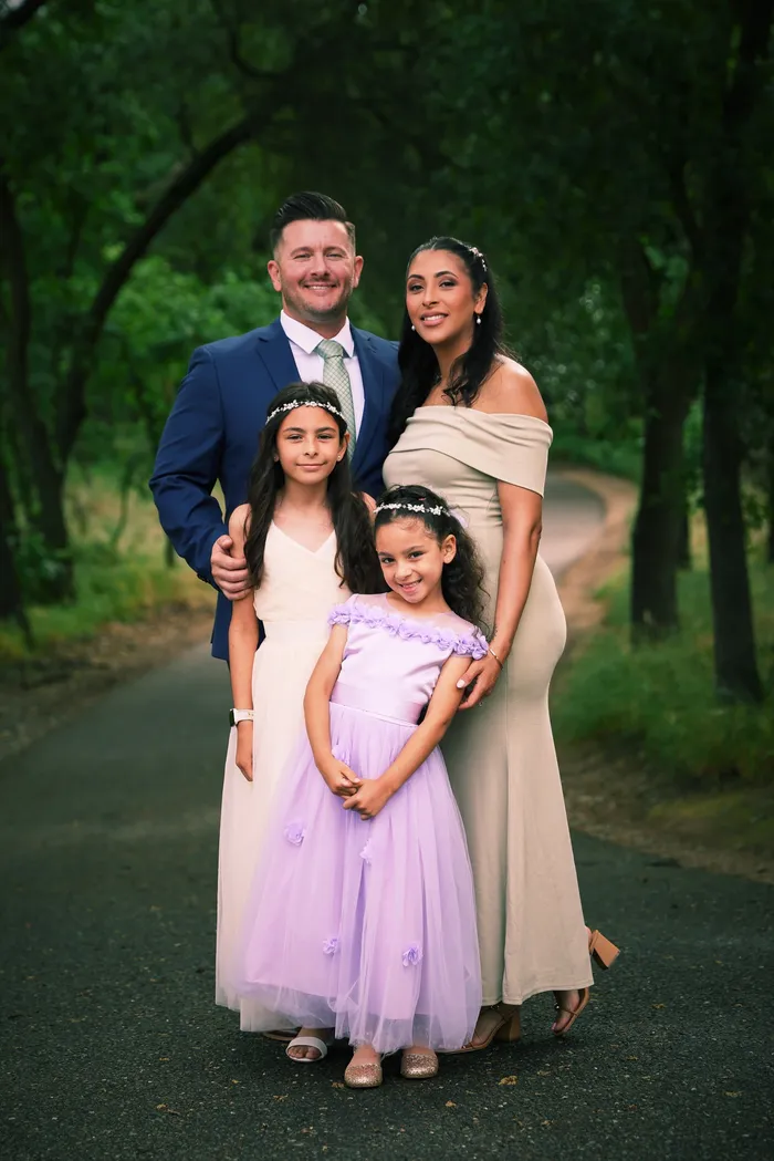 Family portrait of two parents and two young girls in formal dress, on a wooded path