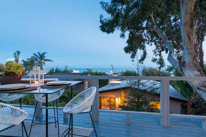 Rooftop deck with dining table and string lights overlooking the coastline at twilight