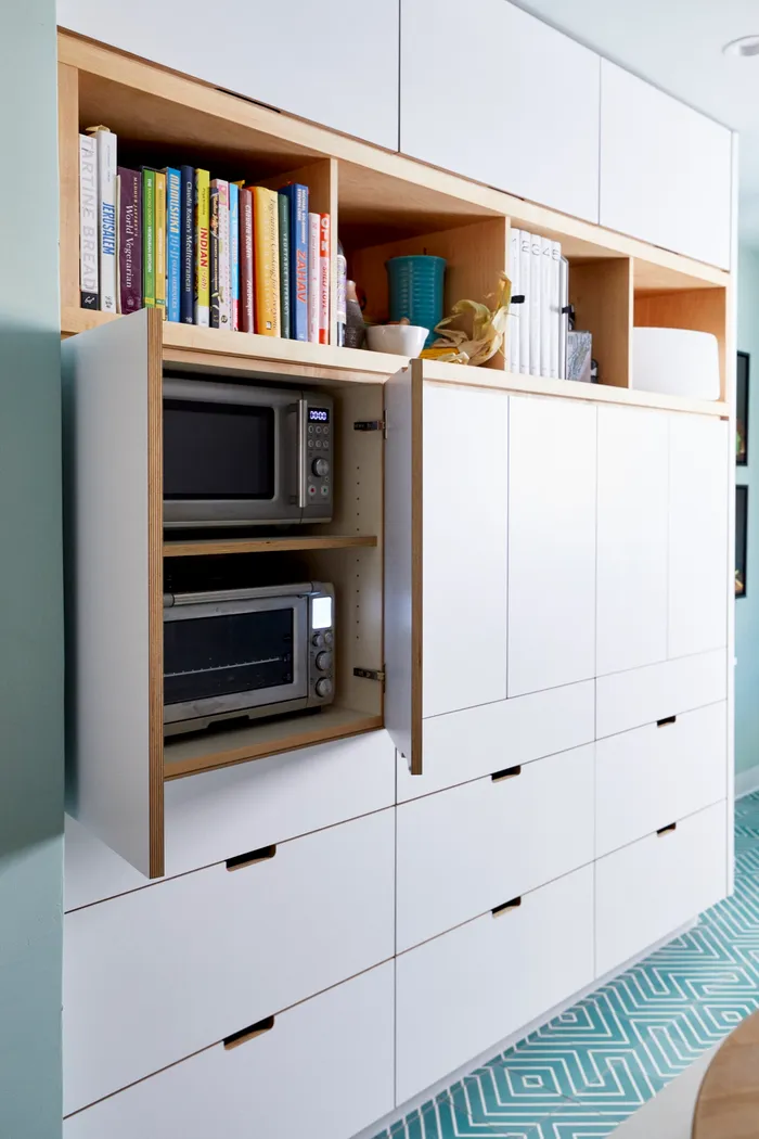 Built-in plywood cabinetry with open cookbook shelving and a pull-out appliance cabinet