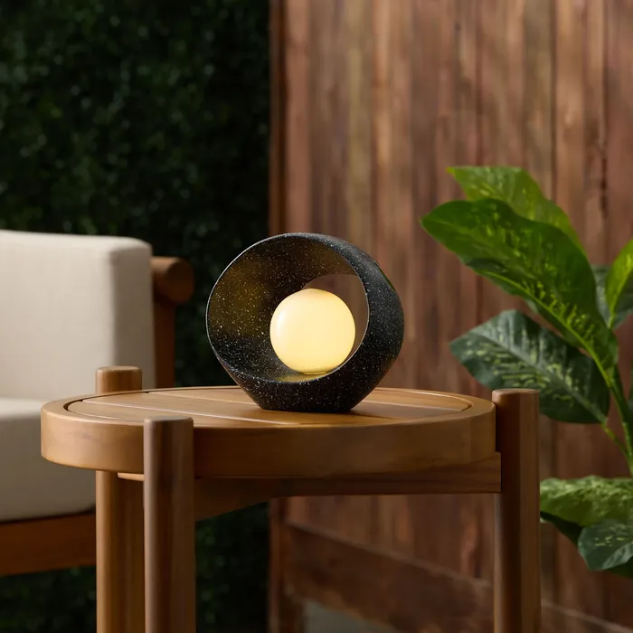 Black speckled ring-shaped table lamp with a glowing glass orb, on an outdoor table